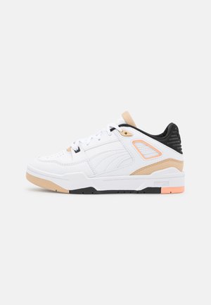 Białe sportowe sneakersy z cholewką ze skóry i siateczki, jasnobeżowe akcenty, czarna pięta i kontrastowa pomarańczowa podeszwa.