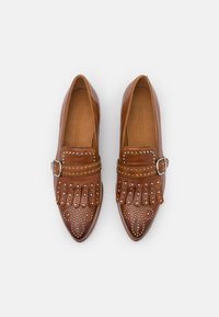 Mocassins en cuir marron à bouts pointus, ornés de clous métalliques et d'une boucle décorative. Détails frangés à l'avant.