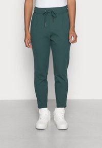 Teal joggerbyxor med dragsko i midjan, sidofickor, tapered ben och subtila veck. Matchas med vita högstövlade sneakers.