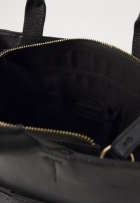 Musta nahkainen olkalaukku, jossa kultainen vetoketju, sileä pinta ja musta kangasvuori. Laukussa on taskuja ja sisäinen logotunniste.