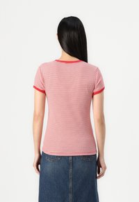 Rot-weiß gestreiftes T-Shirt mit kurzen Ärmeln und rundem Ausschnitt, mit roten Akzenten an den Ärmeln und am Ausschnitt. Trägt einen Jeansrock dazu.