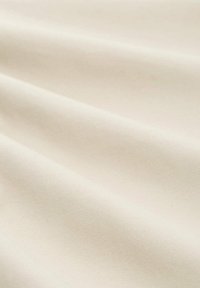 Lichtbeige stof met een zachte textuur, voorzien van subtiele plooien die het gladde oppervlak en de uniforme kleur benadrukken. Geen zichtbare patronen.