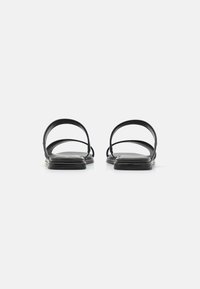 Sandales noires avec deux lanières courbées et une semelle plate, présentant une texture en cuir lisse et un design minimaliste, vues de derrière.