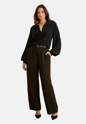 Black long-sleeve blouse with pleats, v-neck, and button detail paired with high-waisted brown wide-leg trousers. Black pointed heels.