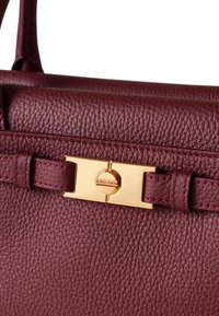 Burgunderfarbene Lederhandtasche mit strukturierten Oberfläche, goldfarbigen Beschlägen und einer Schnallenverschluss. Doppelte Griffe zum Tragen.