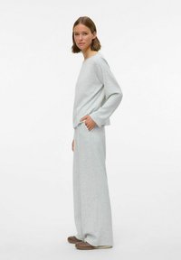 Szary, miękki zestaw odzieży domowej z długimi rękawami, szerokimi spodniami i kieszeniami. Materiał ma gładką fakturę i luźny krój.