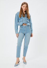 Chaqueta de mezclilla de color azul claro, recortada y con dos bolsillos frontales, combinada con jeans de mezclilla de color azul claro de tiro alto. La modelo lleva unos zapatos de tacón azules.