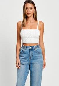 Top corto blanco con patrón de punto texturizado y escote cuadrado, combinado con jeans de tiro alto azul claro que cuentan con una cintura elástica.