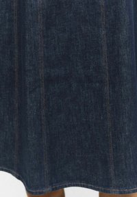 Dżinsowa spódnica w ciemnoniebieskim kolorze z widocznymi pionowymi szwami, charakteryzująca się lekko A-liniowym kształtem i gładką fakturą. Krawędzie są starannie wykończone.