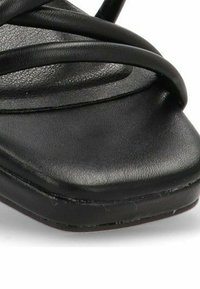 Sandalia negra de tacón con una puntera ancha y cuadrada y múltiples tiras delgadas. Hecha de cuero suave, cuenta con una plantilla acolchada y una suela texturizada.