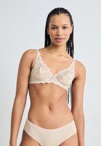 Lace bralette in nude met verstelbare bandjes en golfranden, gecombineerd met bijpassende naadloze bikinislips. Zachte textuur, delicate patroon.