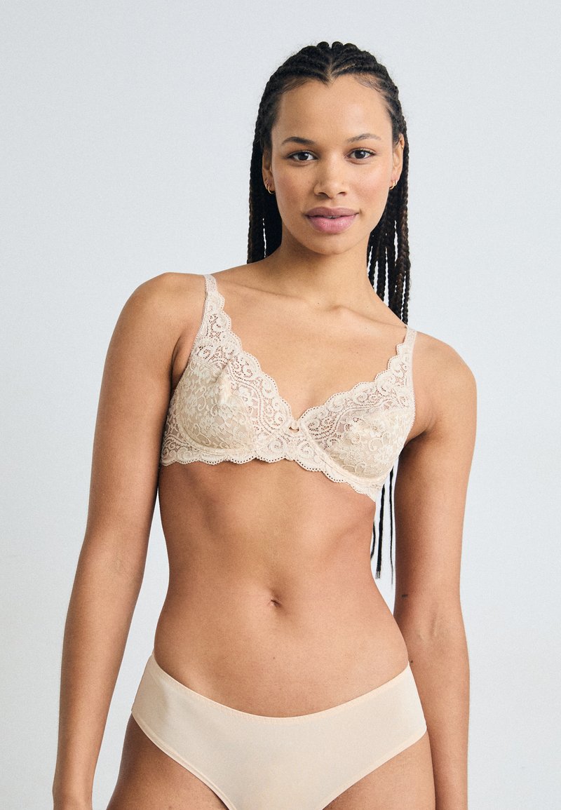 Lace bralette in nude met verstelbare bandjes en golfranden, gecombineerd met bijpassende naadloze bikinislips. Zachte textuur, delicate patroon.