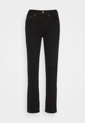 Juodos džinsinės kelnės su tiesiu kirpimu, su suplėšyta kelių detale, penkiomis kišenėmis ir vario dekoratyviniais akcentais ant diržo.