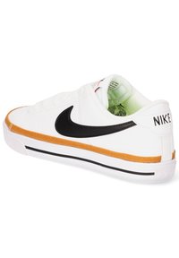 Zapatilla blanca con el swoosh negro de Nike, acento naranja en la suela, parte superior blanca texturizada y franjas negras en la base. Diseño de punta redondeada.