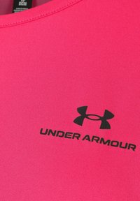 Camiseta deportiva rosa con un acabado texturizado, escote redondo y logotipo negro de Under Armour en la parte frontal.