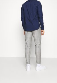 Mörkblå långärmad skjorta med knappar bak, i kombination med ljusgrå rutiga byxor och vita sneakers, med en slim fit-design.