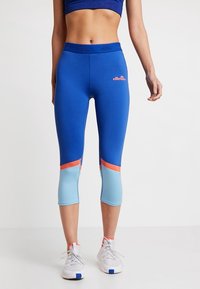 Modré capri legíny s světle modrými a korálovými akcenty, vyrobené z elastického materiálu. Obsahují logo na pase a design s barevnými bloky.