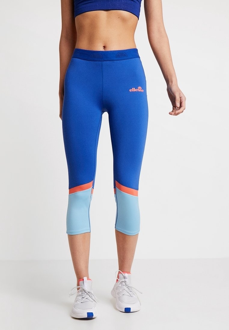 Modré capri legíny s světle modrými a korálovými akcenty, vyrobené z elastického materiálu. Obsahují logo na pase a design s barevnými bloky.