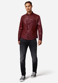 Bordeaux lädertröja med knapp-ner krage, två bröstfickor och tryckknappar, i kombination med mörka jeans och svarta sneakers.