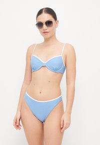 Lyseblå bikini med polstret topp med hvit kant og justerbare stropper, sammen med matchende høy midje-bukser.