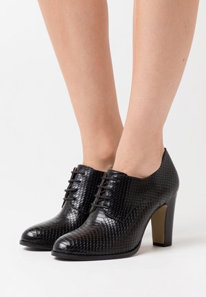 Bottines à talons noirs avec un motif texturé imitation peau de serpent, dotées de lacets et d'une finition lisse. Les talons ont une hauteur modérée.