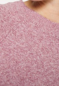 Gestrickter Pullover in sanftem Rosa, mit rundem Ausschnitt, dezenter Textur und einer Mischung aus hellen und dunklen Fasern für Tiefe.