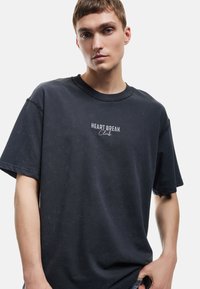 Sort bomulds t-shirt med en afslappet pasform, korte ærmer og rund halsudskæring. Har "HEART BREAK Club" broderet på brystet.