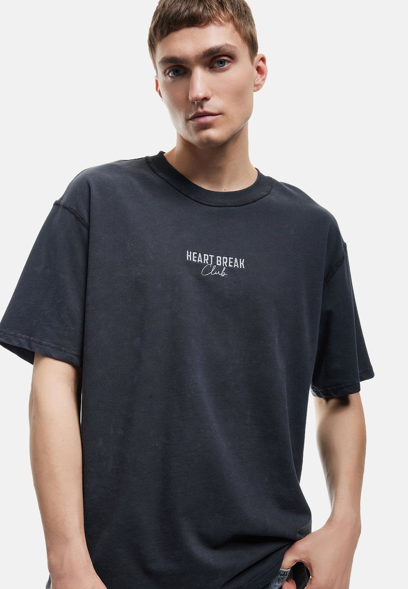 Sort bomulds t-shirt med en afslappet pasform, korte ærmer og rund halsudskæring. Har "HEART BREAK Club" broderet på brystet.