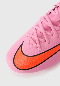 Roosa jalgpalliking, millel on tekstureeritud pind, mustad paelad ja suur oranž Nike swoosh, mis on musta äärisega. Suurendatud vaade.