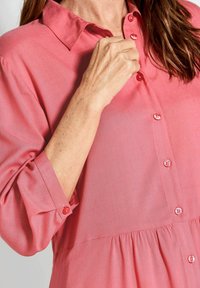 Camicia button-up rosa con colletto, dotata di maniche arrotolate e orlo arricciato. Tessuto liscio con bottoni abbinati lucidi.
