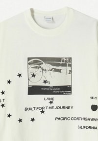 T-shirt bianco in cotone con una grafica centrale nera di un volante, testo sovrapposto e stelle nere sparse.
