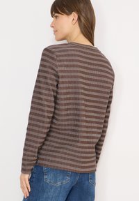 Haut à manches longues marron avec des rayures horizontales blanches et marron clair, col rond et coupe décontractée, assorti à un jean en denim bleu.