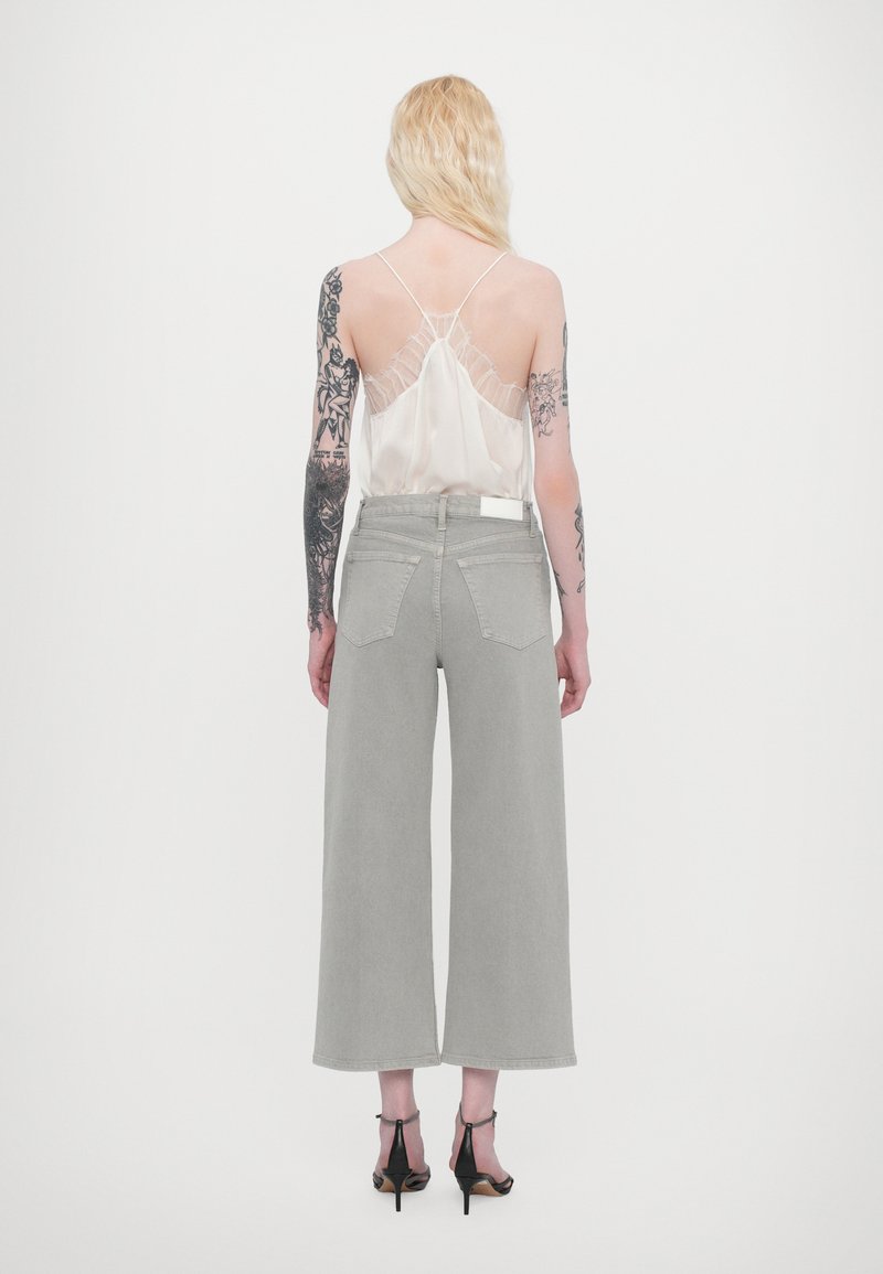 Light gray wide-leg jeans with a high waist, paired with a translucent cream camisole featuring lace trim and thin straps. Black heels.