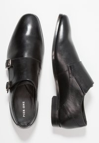 Un paio di scarpe eleganti in pelle nera con doppia fibbia in argento, una mostrata dall'alto e l'altra di profilo.