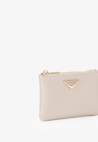 Portafoglio zip in pelle beige con un accento logo triangolare in tono oro. Superficie texture e bordi lisci, con chiusura a zip dorata.