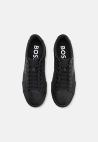 Svarta sneakers med en strukturerad ovandel, rund tå och kontrasterande slät läder. Har svarta snören och "BOSS"-logotyp på sulorna.