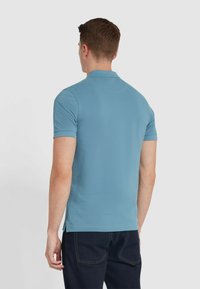 Polo bleu clair à manches courtes, avec un col classique et des fentes latérales, associé à un jean en denim foncé. Texture lisse, design ajusté.