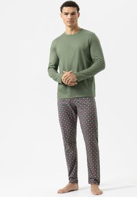 Olijfgroen langemouwtop gecombineerd met gestreepte pyjamabroek met cirkelvormige ontwerpen in rood en blauw op een grijze achtergrond.