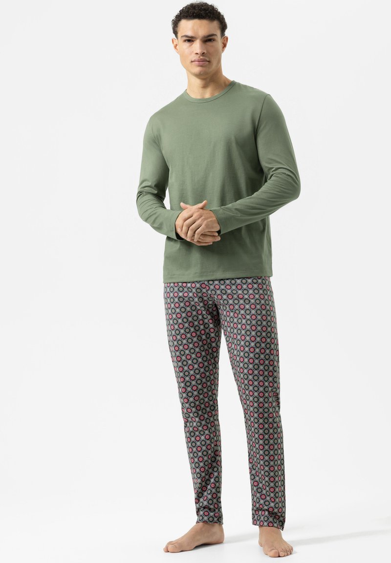 Olijfgroen langemouwtop gecombineerd met gestreepte pyjamabroek met cirkelvormige ontwerpen in rood en blauw op een grijze achtergrond.