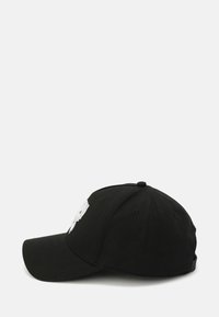 Black cap with a curved bill, textured fabric, and white embroidered logo on the front. Features eyelets for breathability and an adjustable strap.