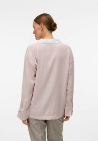 Randig långärmad blus i rosa och vitt tyg, med vit krage, manschettdetaljer och en avslappnad passform. Detaljer inkluderar knäppta manschetter.