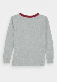 Camisa de manga larga en algodón gris claro con cuello burdeos. Presenta costuras sencillas y puños ajustados. Etiqueta visible en la parte inferior izquierda.