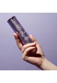 Lila Farbverlauf zylindrische Flasche, die in einer Hand gehalten wird, mit einem schwarzen Deckel und weißem Text, der den Produktnamen und die Marke angibt. Glatte Oberfläche.
