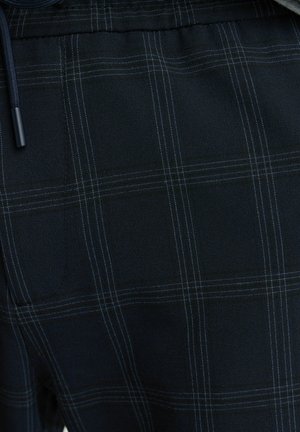 Granatowy materiał z subtelnym wzorem w kratę i jasnoniebieskimi liniami. Materiał wydaje się miękki o gładkiej fakturze. Zawiera detal ze sznurkiem.