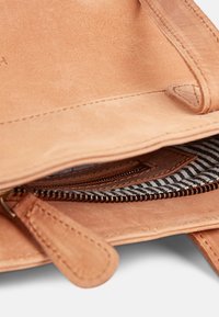 Tan leather bag interior with a smooth finish; features a zippered pocket with a striped fabric lining. Stitched edges are visible.