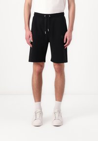 Black athletic shorts with drawstring waist, side stripe accents, and side pockets, paired with white sneakers and light gray socks.
