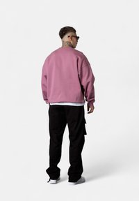 Oversized pink sweatshirt with ribbed cuffs, worn over a white shirt, paired with black cargo pants and white sneakers.