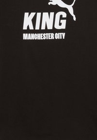 Camiseta negra con "KING" y "MANCHESTER CITY" impresos en blanco. Presenta un logo de gato estilizado encima del texto. Material de algodón.