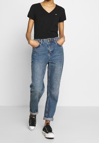 Černé tričko s véčkovým výstřihem spárované se světle modrými, vysokými džínami, ohrnutými na manžetách, a černými nízkými teniskami s bílou podrážkou.