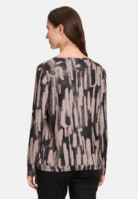 Langärmlige Bluse aus schwarzem und beigem Stoff mit einem abstrakten Muster, rundem Ausschnitt und lockerer Passform mit seitlichen Schlitzen für mehr Komfort.